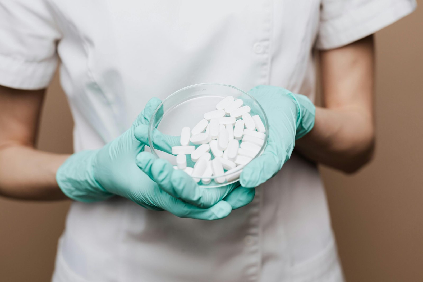 Close-up of a healthcare professional holding white pills in a petri dish.