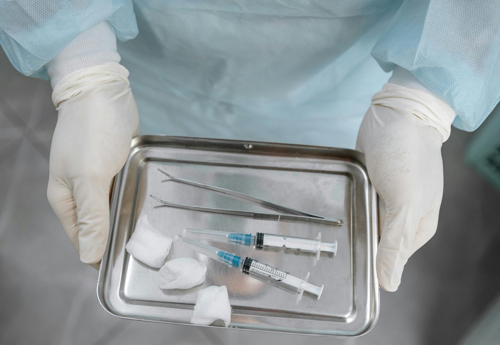 Close-up of a medical professional with syringes, tweezers, and gauze on a steel tray.