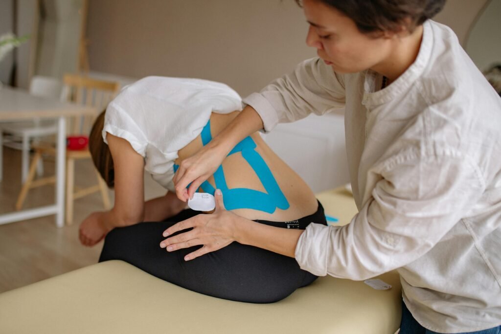 A therapist applies blue kinesiology tape to a patient's back in a clinical setting.